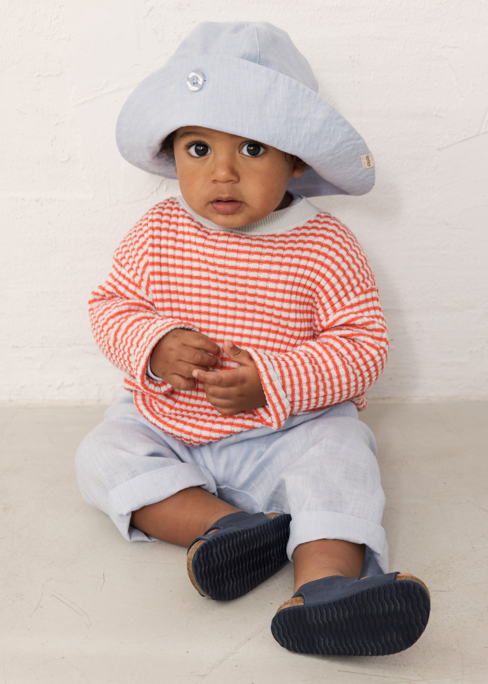 Baby wearing light blue pants, striped shirt, and sun hat.