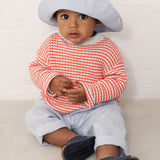 Baby wearing light blue pants, striped shirt, and sun hat.