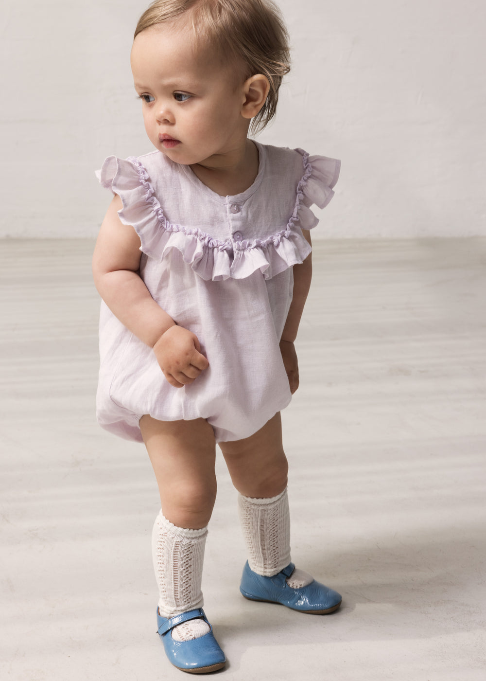 Baby wearing light lavender dress with short sleeves and ruffled details.