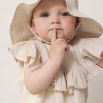 Baby wearing a beige summer hat and matching dress.