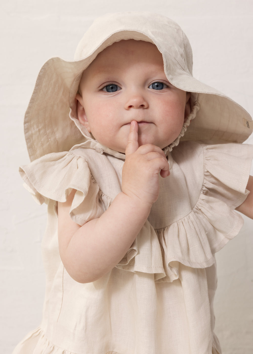 Baby wearing a sleeveless beige top with ruffles and a sunhat.