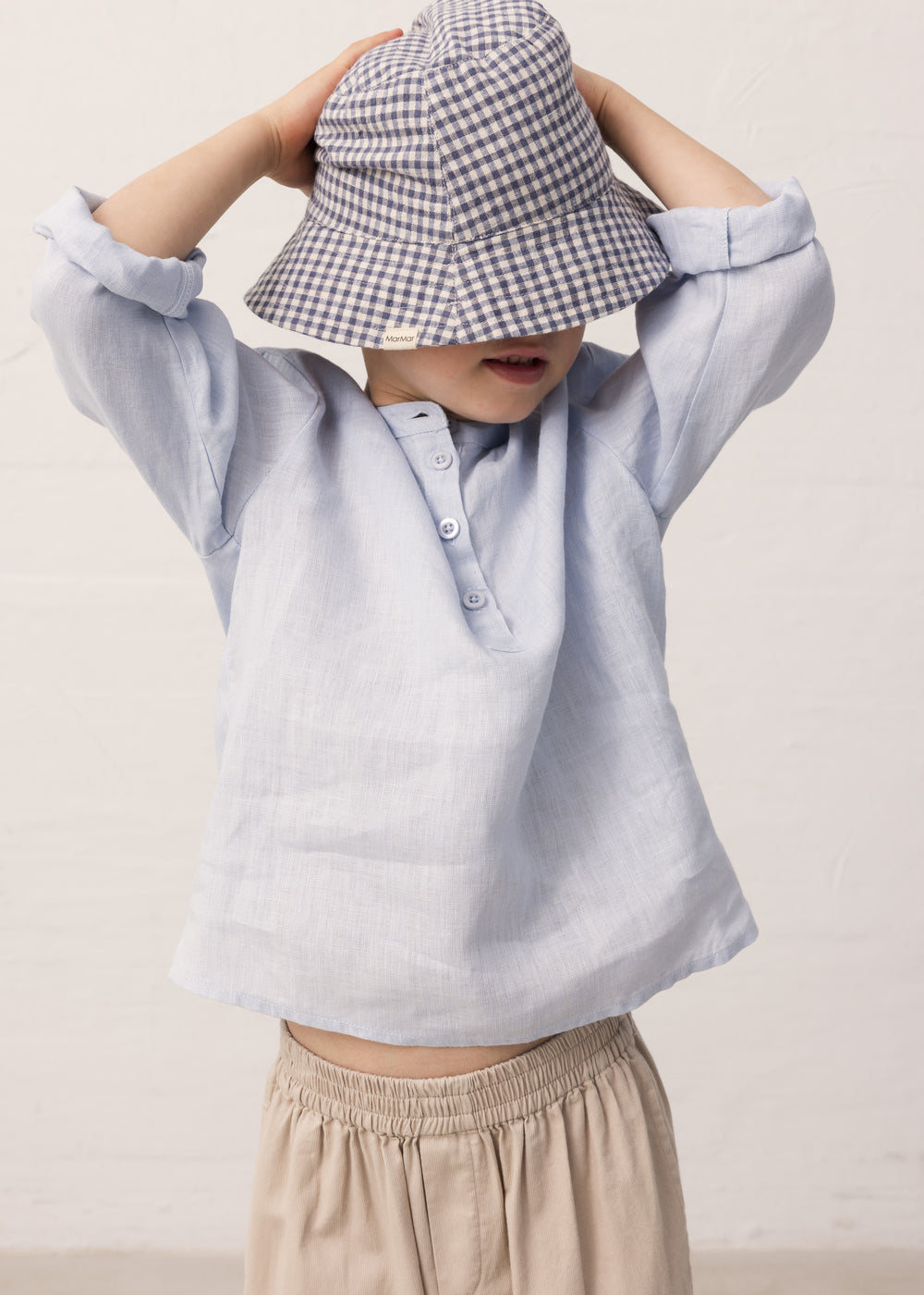 Boy wearing a long-sleeved light blue shirt, beige pants, and a sun hat.