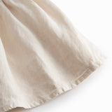 Sleeveless beige dress for children with wide straps and flaps on the shoulder and a smock at the back.