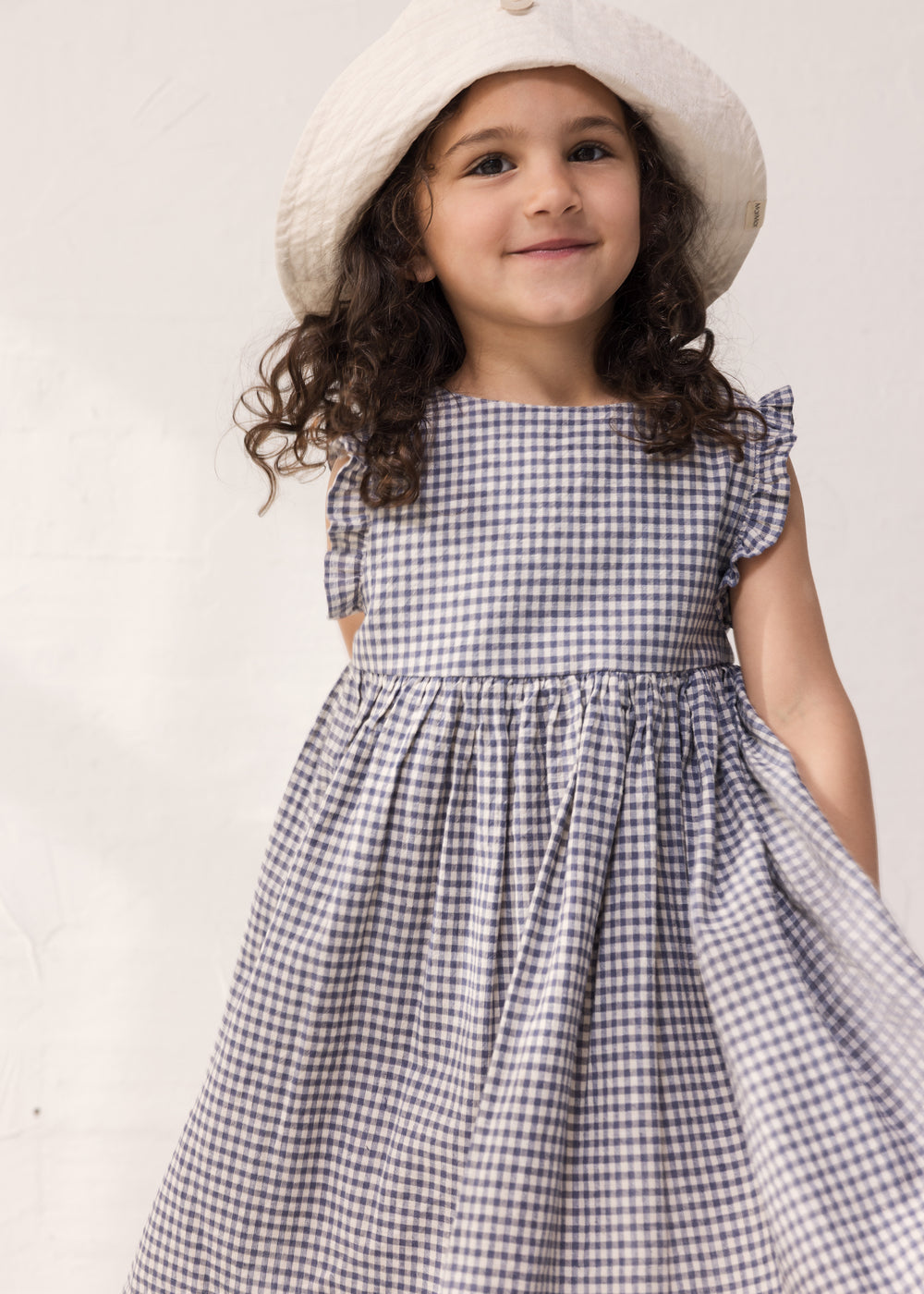 Child wearing a ternet dress with flared sleeves and a hat.