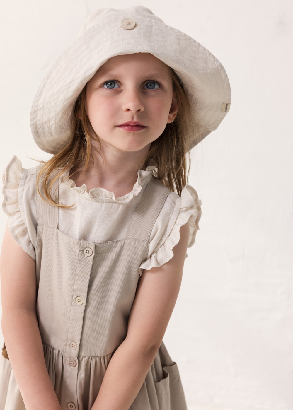 Child wearing a light dress with puffed sleeves and a hat in matching color.
