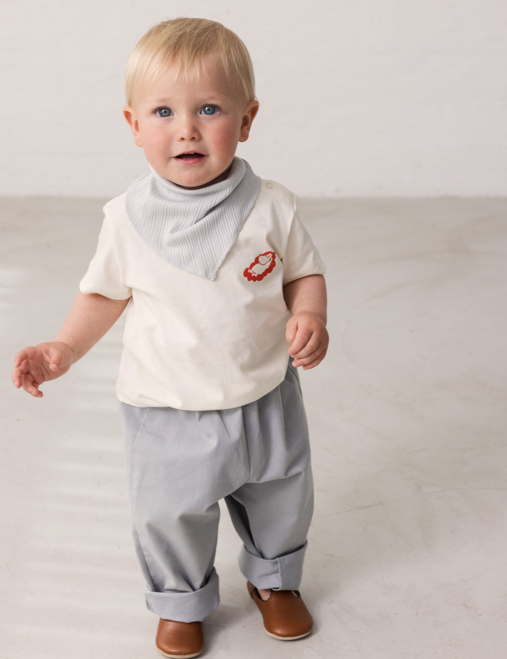 Baby wearing a white T-shirt with Mumin print and light pants.