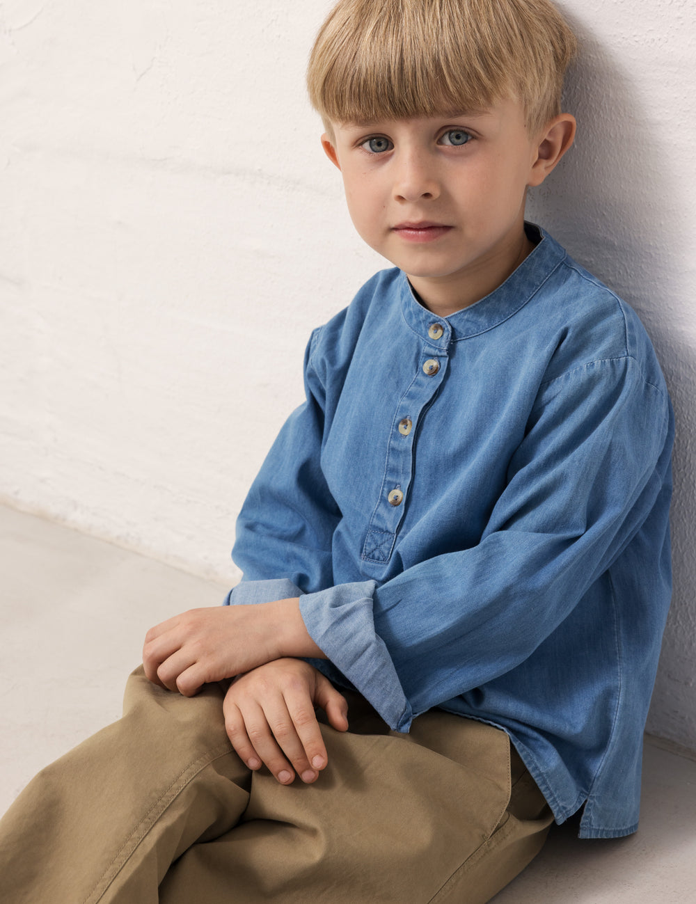 A child wearing a blue denim shirt and green pants.