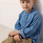 A child wearing a blue denim shirt and green pants.