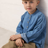 A child wearing a blue denim shirt and green pants.