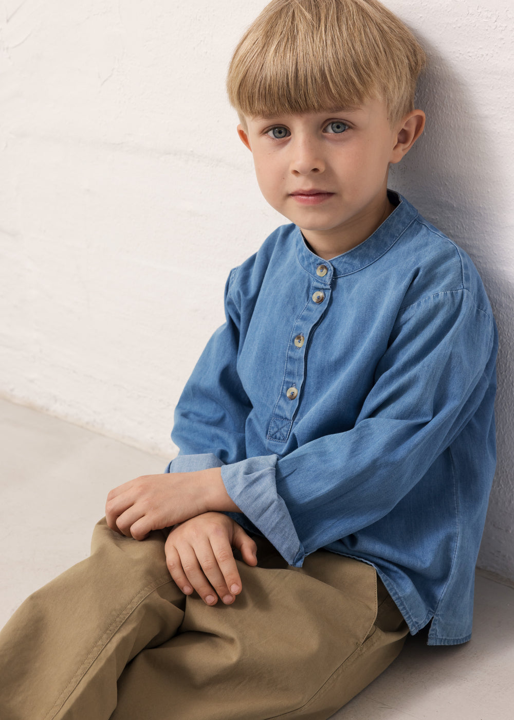 Child wearing a blue denim shirt and brown pants.