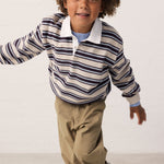 Child wearing a striped sweat polo and brown pants.