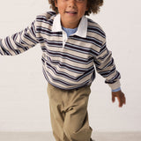 Child wearing a striped sweat polo and brown pants.