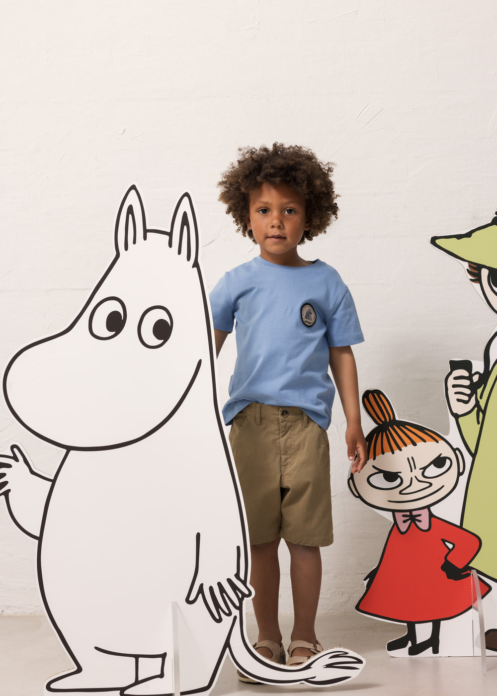 Child wearing a blue T-shirt and green shorts with a Moomin figure.