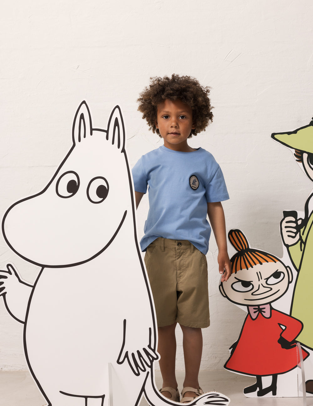 Child wearing a light blue T-shirt and khaki shorts with Moomin figures.