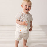 Baby wearing light shorts with embroidered fruits and a matching top.
