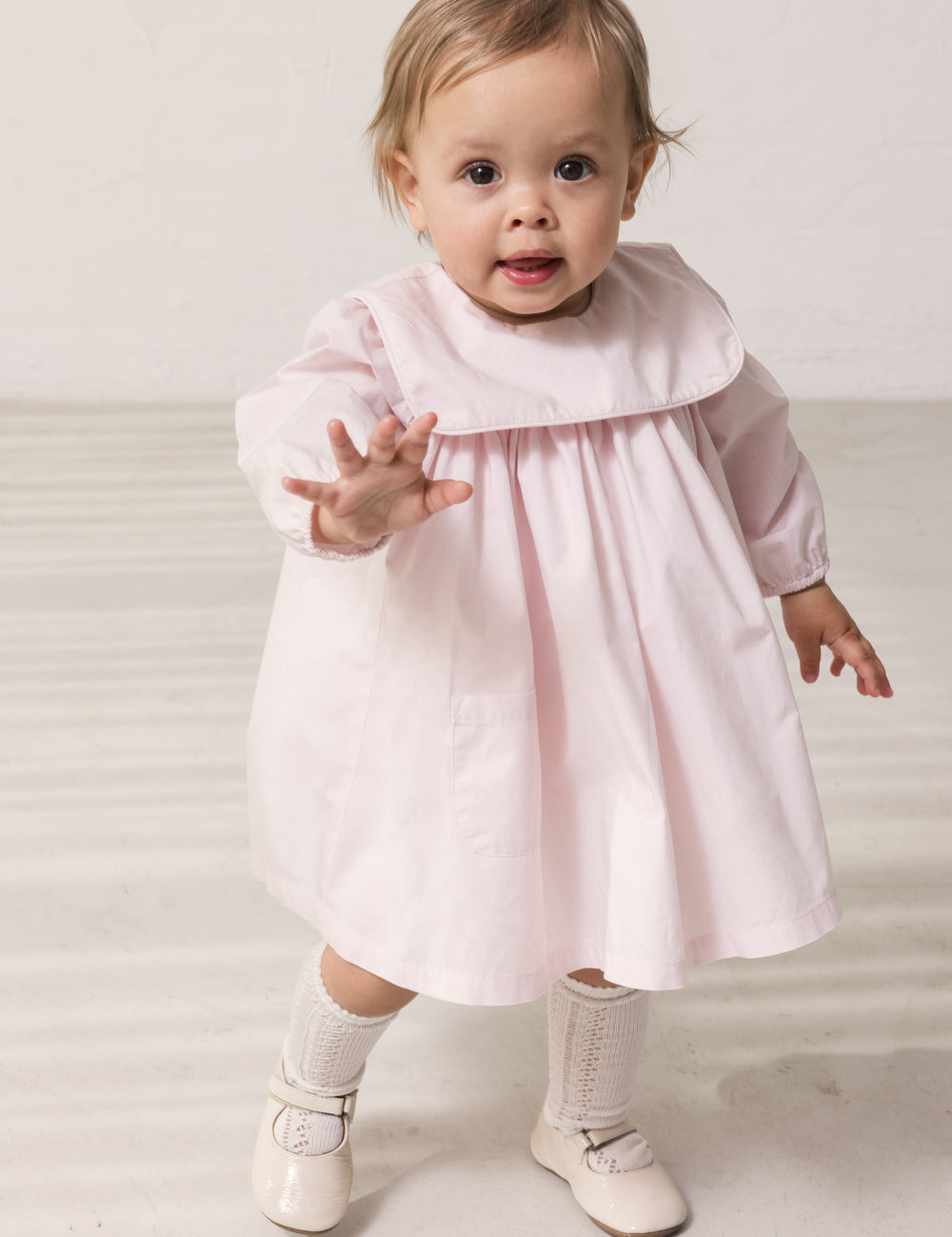 Baby wearing a bright red dress with a collar and long sleeves.