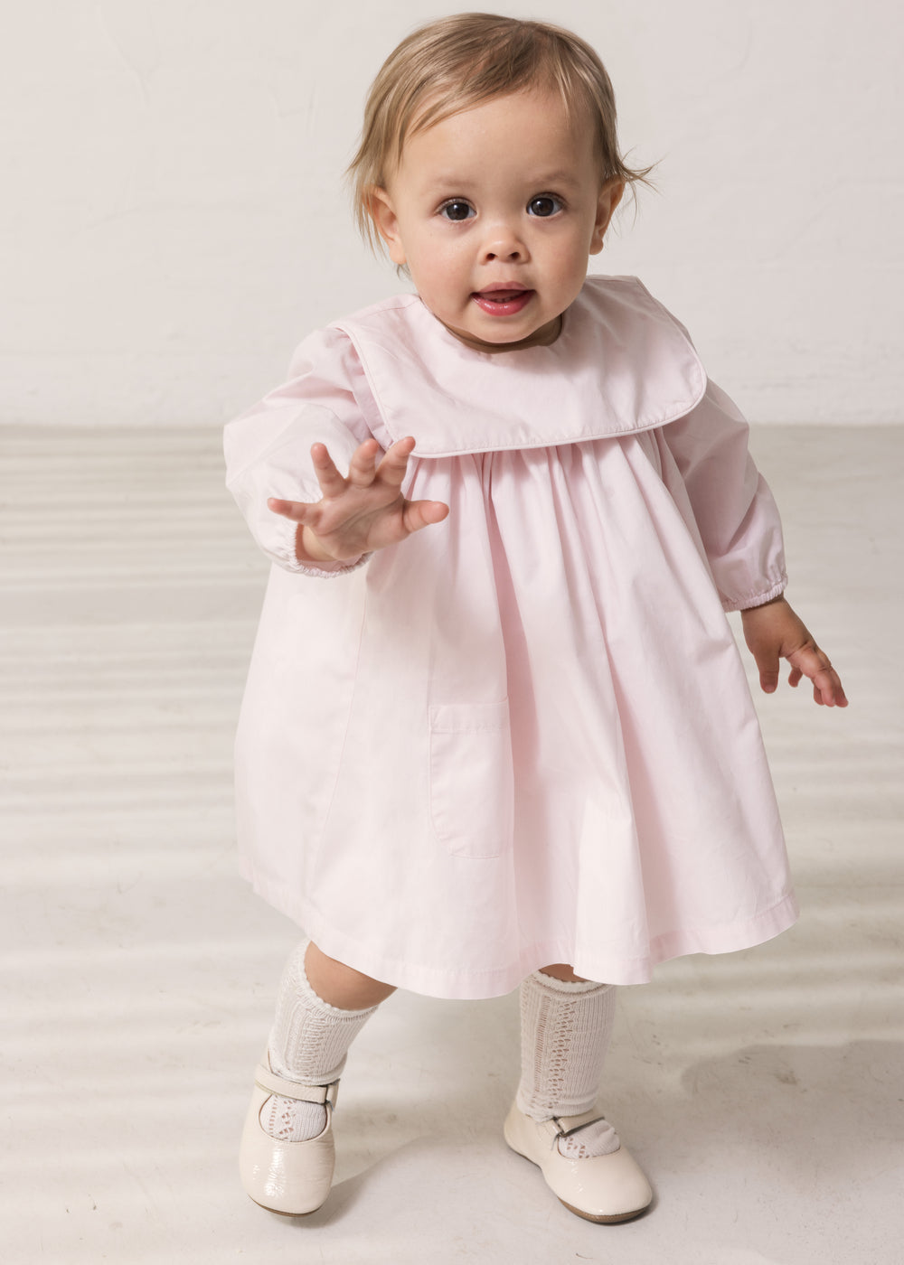 Baby wearing a bright red dress with a collar and long sleeves.