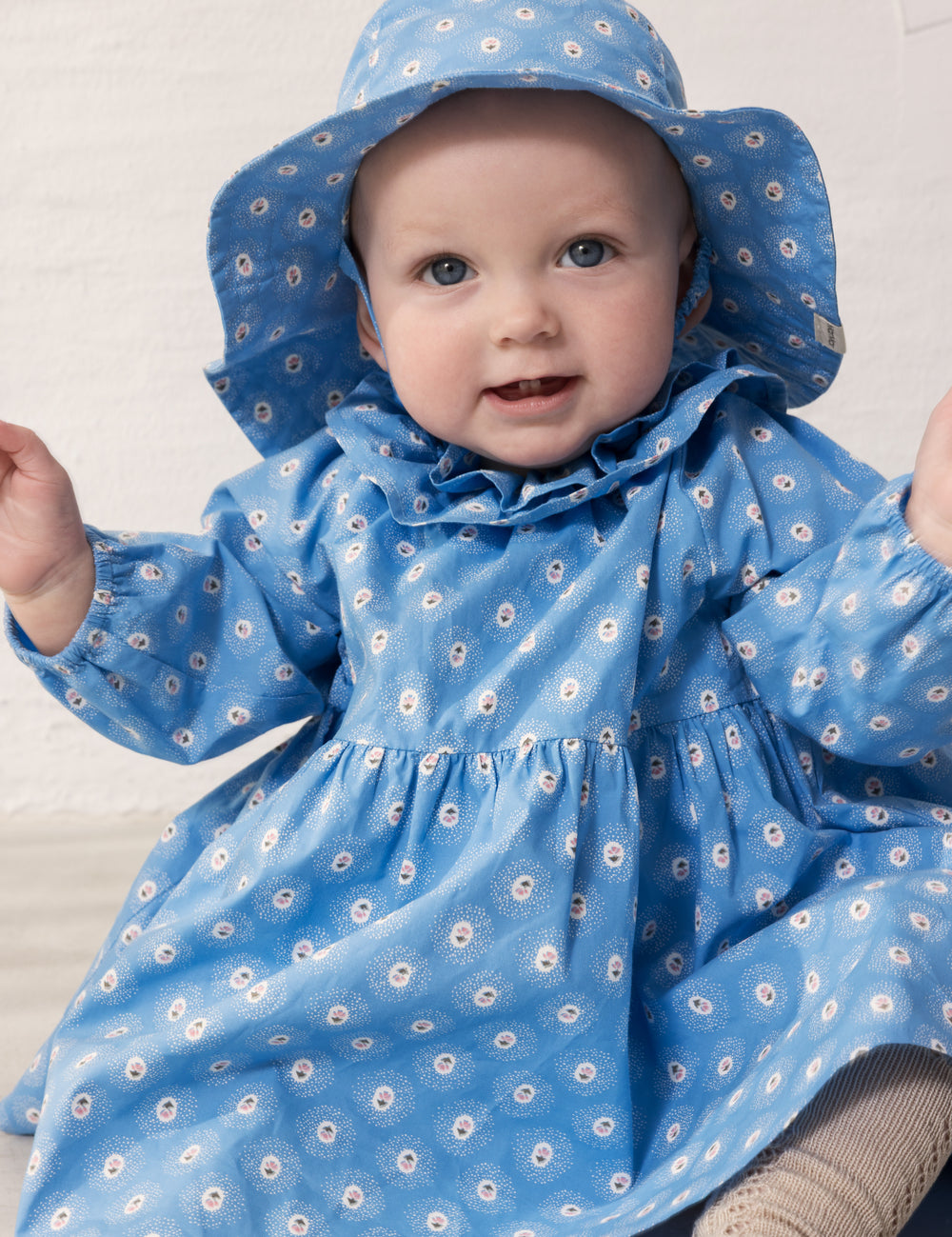 Baby wearing a blue floral dress and matching sunhat.