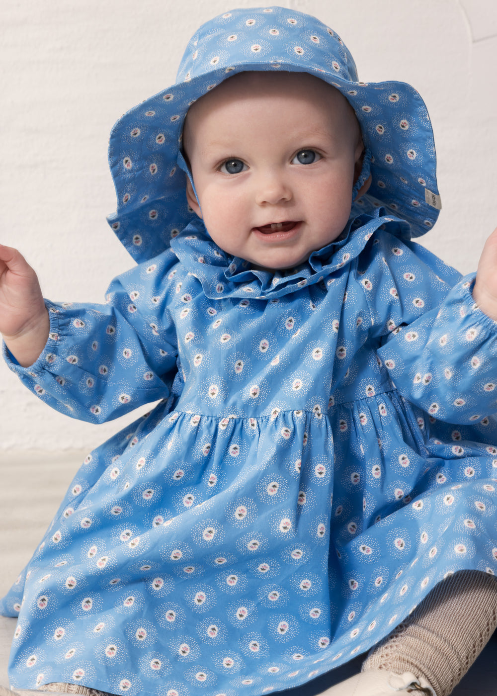 Baby wearing a blue floral dress and matching sunhat.
