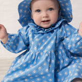 Baby wearing a blue dress with a floral print and matching sunhat.
