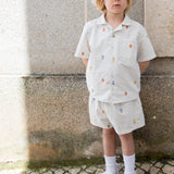 Children wearing a bright set with a shirt and shorts featuring fruit embroidery and a sun hat.