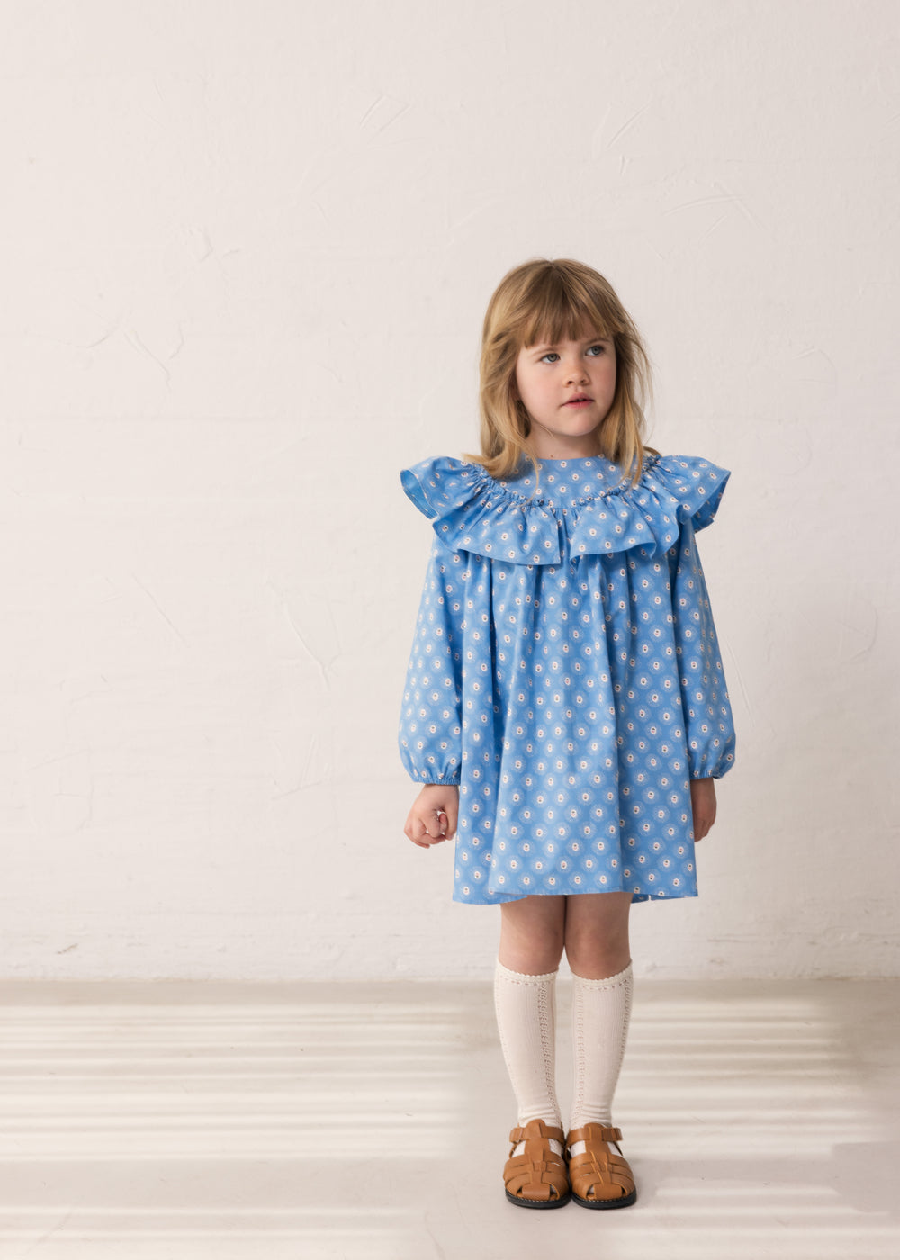 Child wearing a blue dress with a floral print and lace detail.