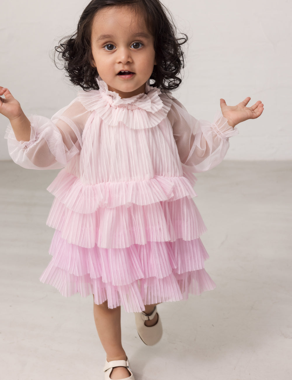 Wearing a bright red long-sleeved baby dress in pleated tulle with multiple layers.