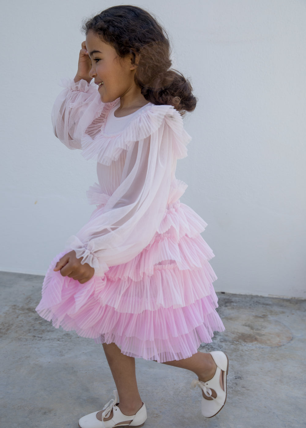 Wearing a long-sleeved, bright red dress in pleated fabric with multiple layers.