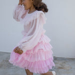 Wearing a long-sleeved, bright red dress in pleated fabric with multiple layers.