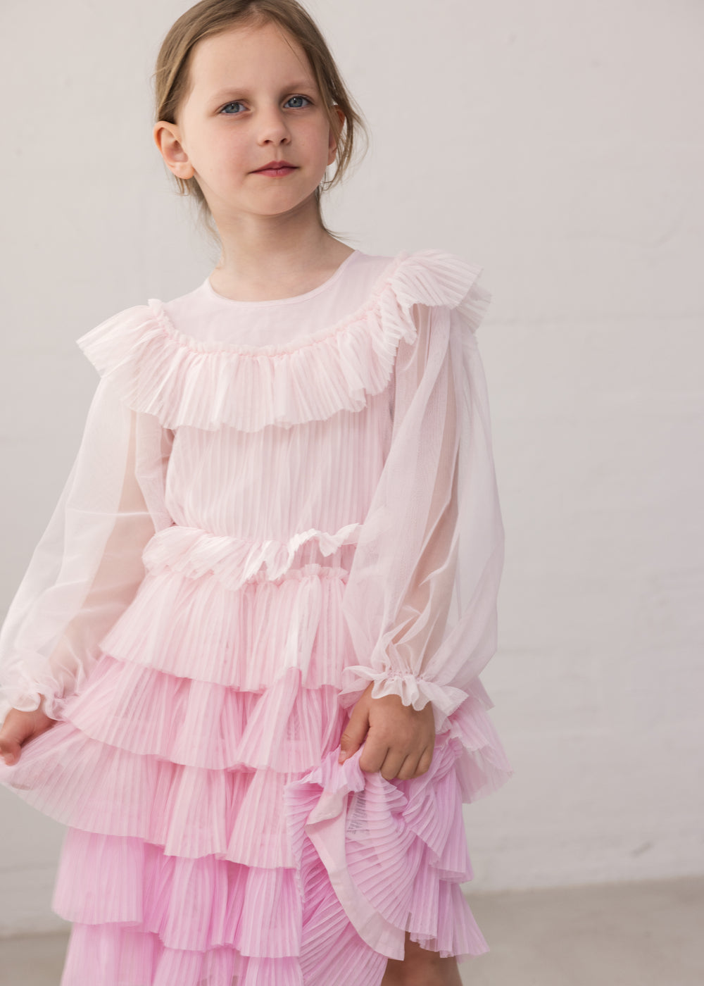 Wearing a long-sleeved, bright red dress in pleated fabric with multiple layers.
