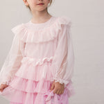 Wearing a long-sleeved, bright red dress in pleated fabric with multiple layers.