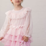 Wearing a long-sleeved, bright red dress in pleated fabric with multiple layers.