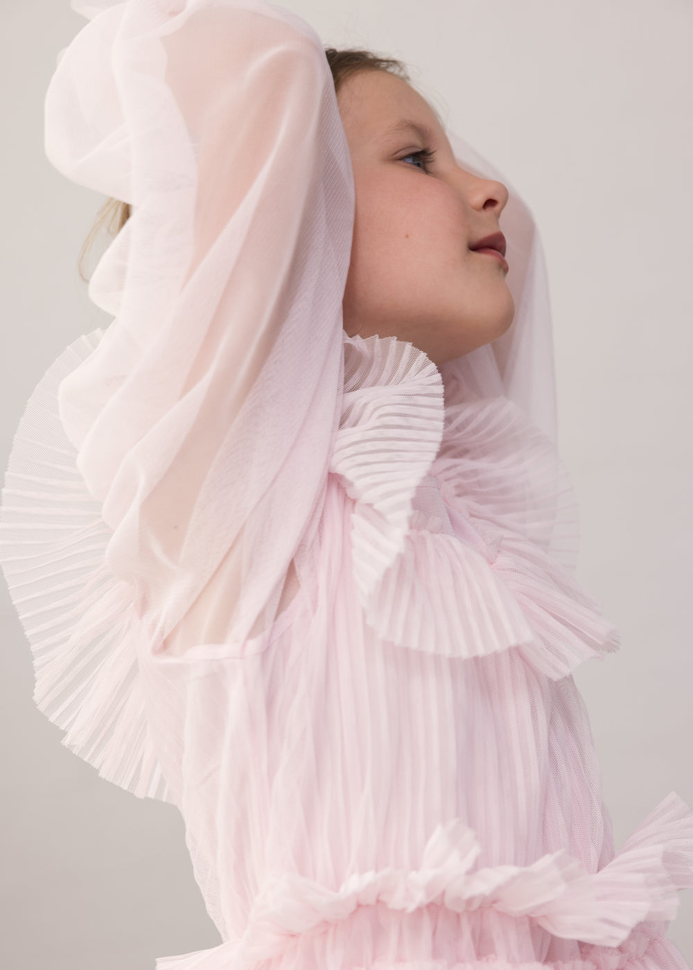 Wearing a long-sleeved, bright red dress in pleated fabric with multiple layers.