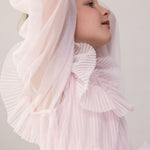 Wearing a long-sleeved, bright red dress in pleated fabric with multiple layers.