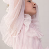 Wearing a long-sleeved, bright red dress in pleated fabric with multiple layers.