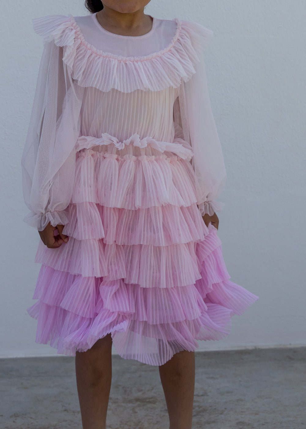 Children wearing a bright red long-sleeved dress in pleated fabric with multiple layers.