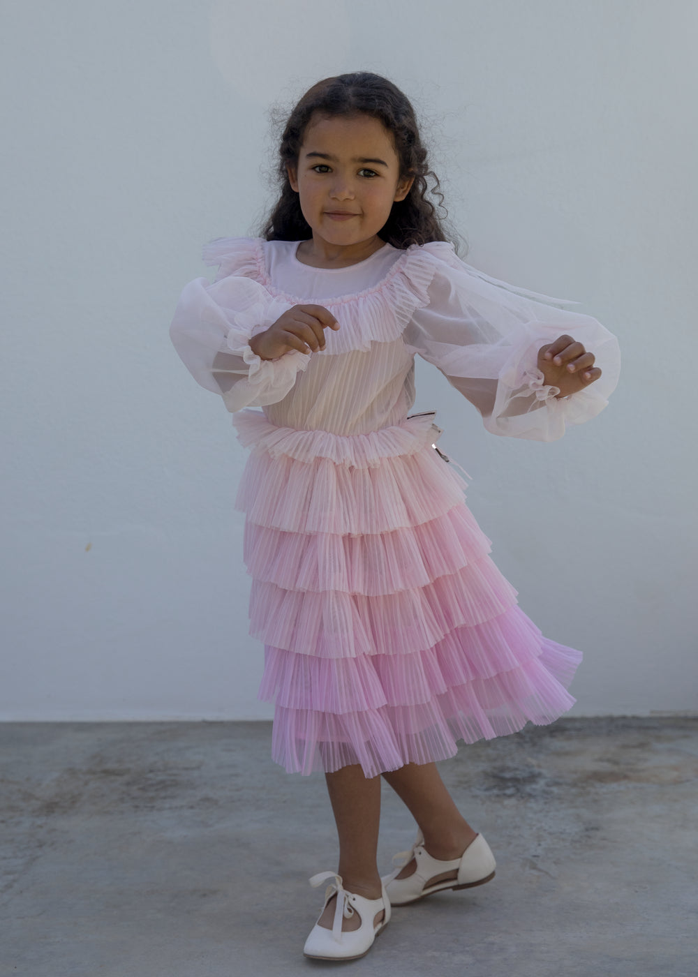 Wearing a long-sleeved, bright red dress in pleated fabric with multiple layers.