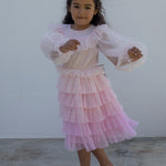 Wearing a long-sleeved, bright red dress in pleated fabric with multiple layers.