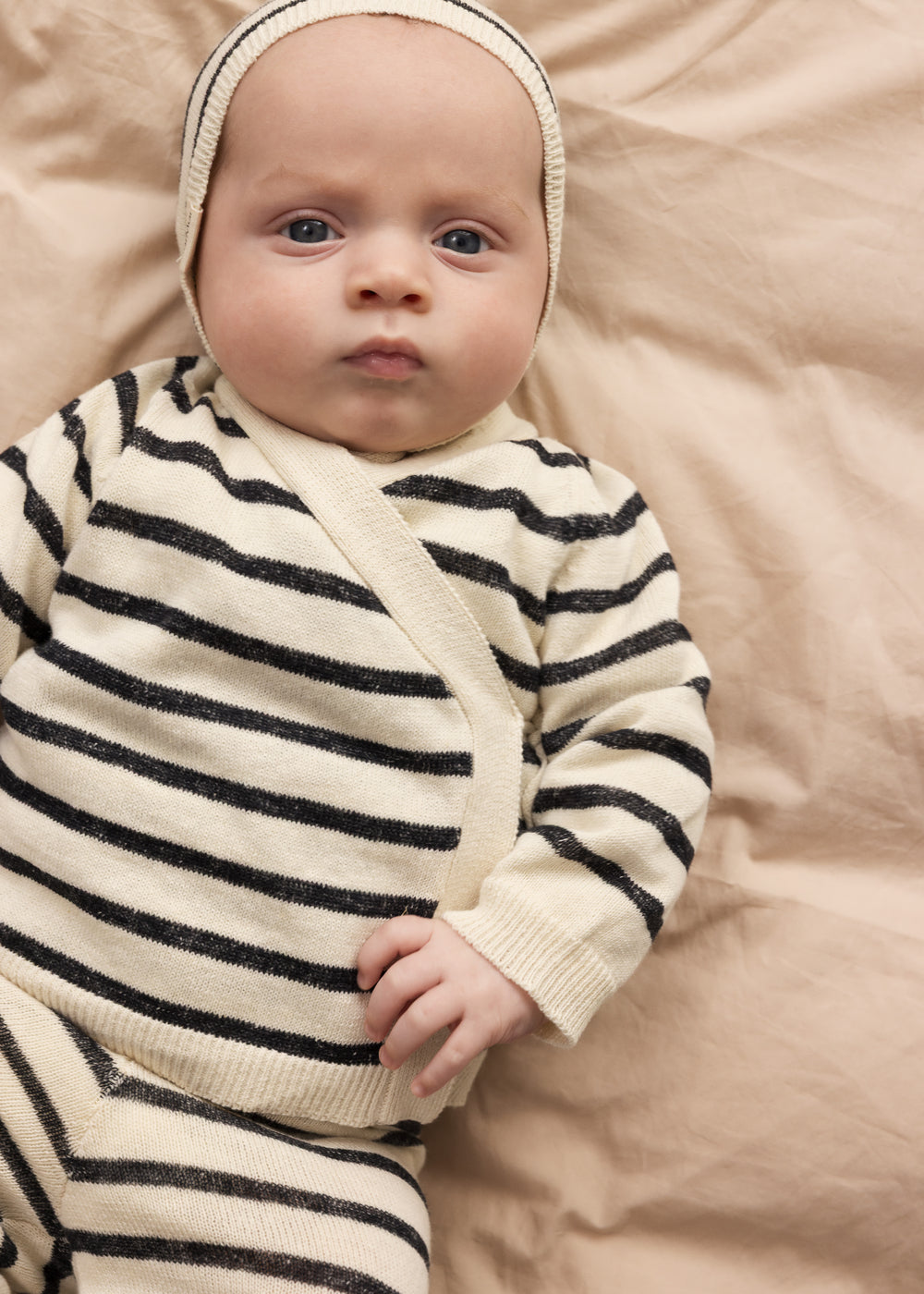 Baby wearing a striped cardigan with stripes and toggle closure, matching pants and hat.
