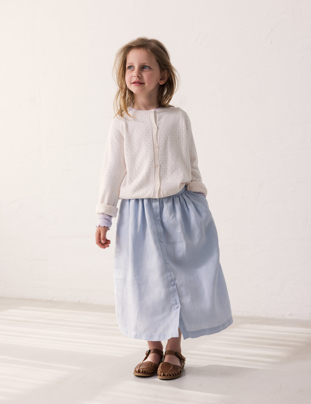 Child wearing a white cardigan and light blue pants with buttons.