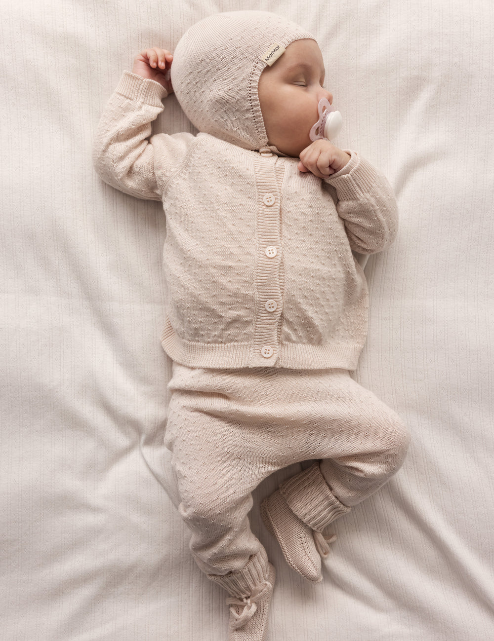 Baby wearing a red knitted set with pants and hat.