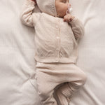 Baby wearing a knitted set in raw white with cardigan, pants, and hat.