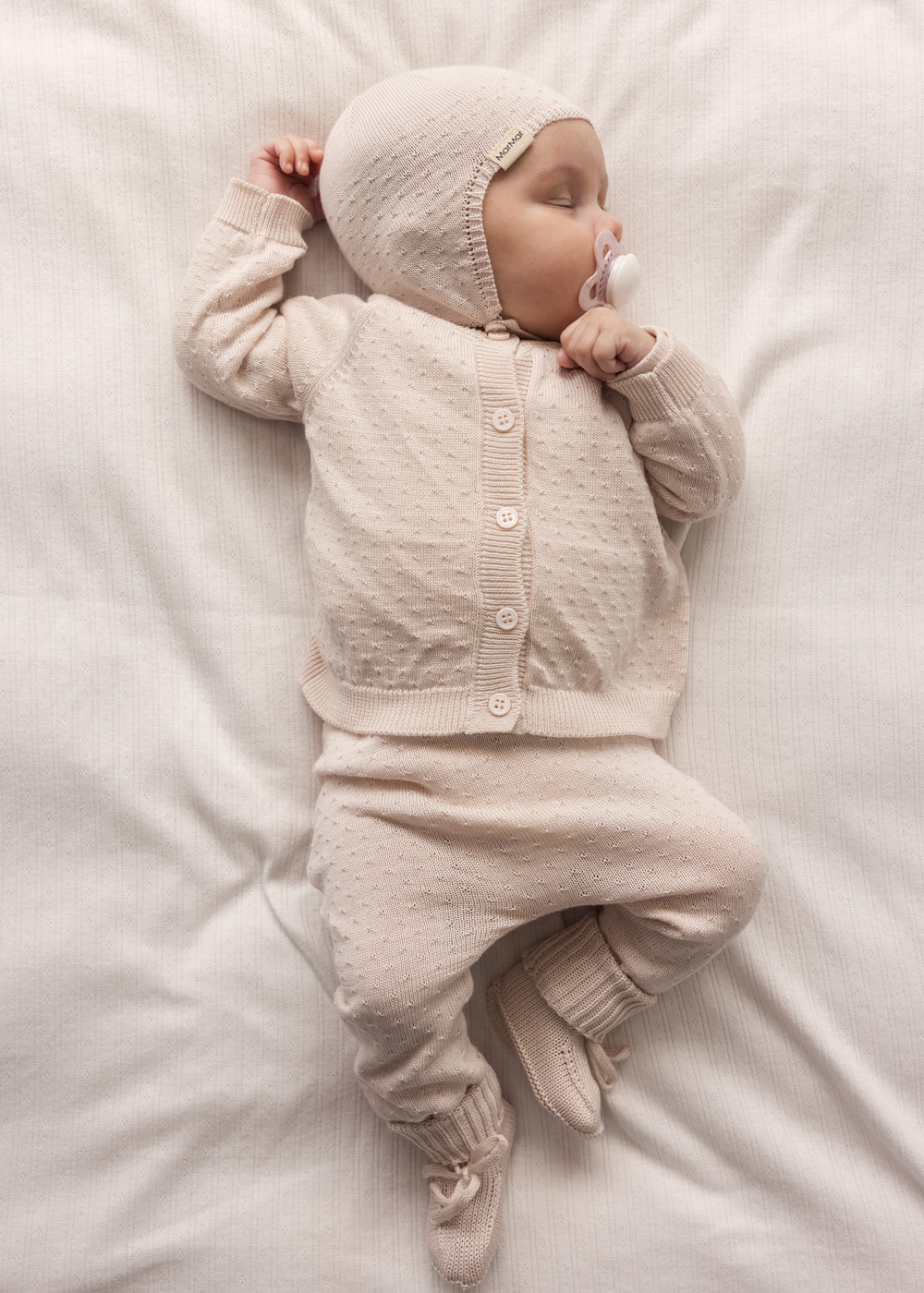 Baby wearing a red knitted set with matching hat and booties.