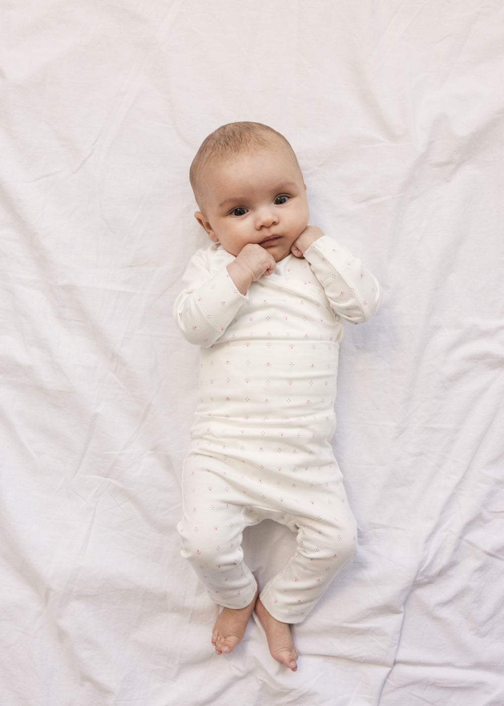 Baby in white baby trousers and bodysuit with small flowers