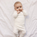 Baby in white baby bodysuit and trousers with small flowers