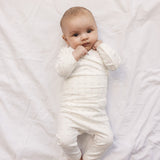 Baby in white baby bodysuit and trousers with small flowers