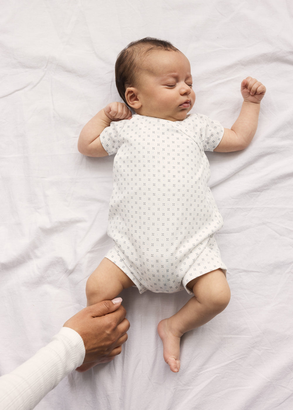 Baby sleeping in white footless sleepsuit with fine pattern