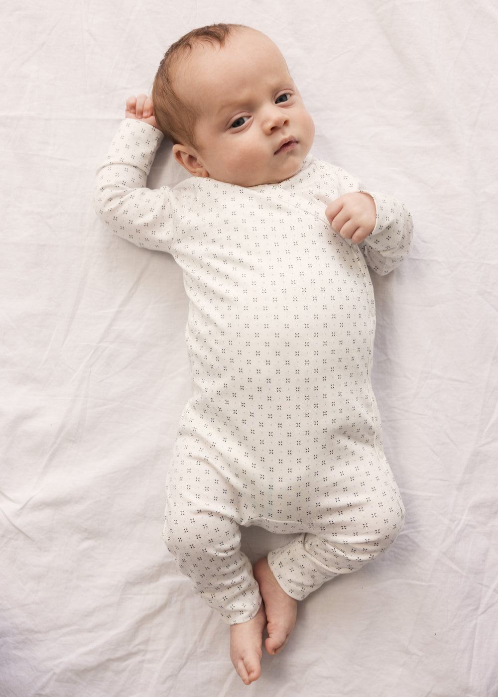 Baby in white full-body suit with wrap-around closure and a fine pattern