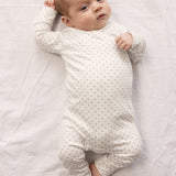 Baby in white full-body suit with wrap-around closure and a fine pattern