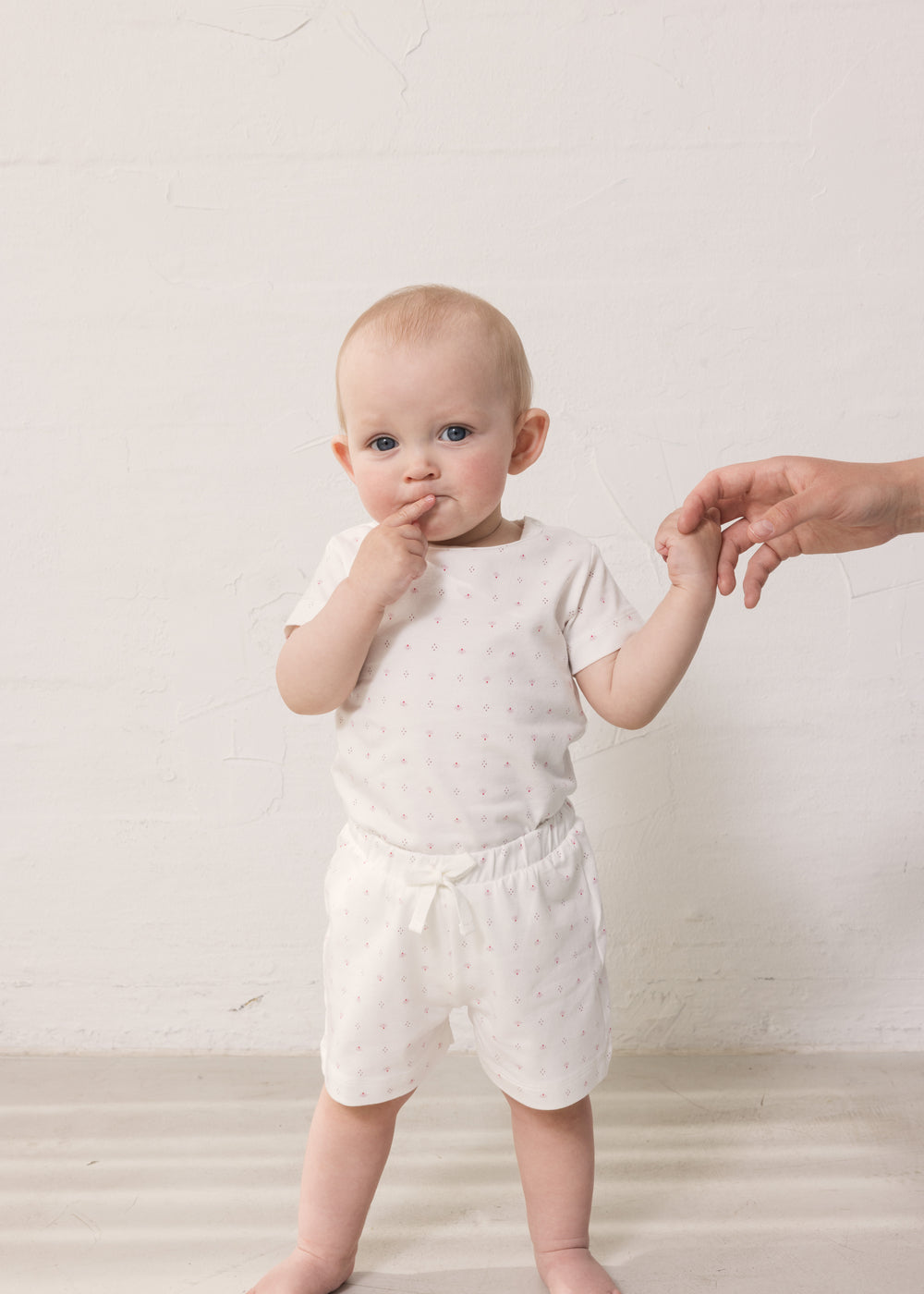 Baby in white shorts and bodysuit with small flowers